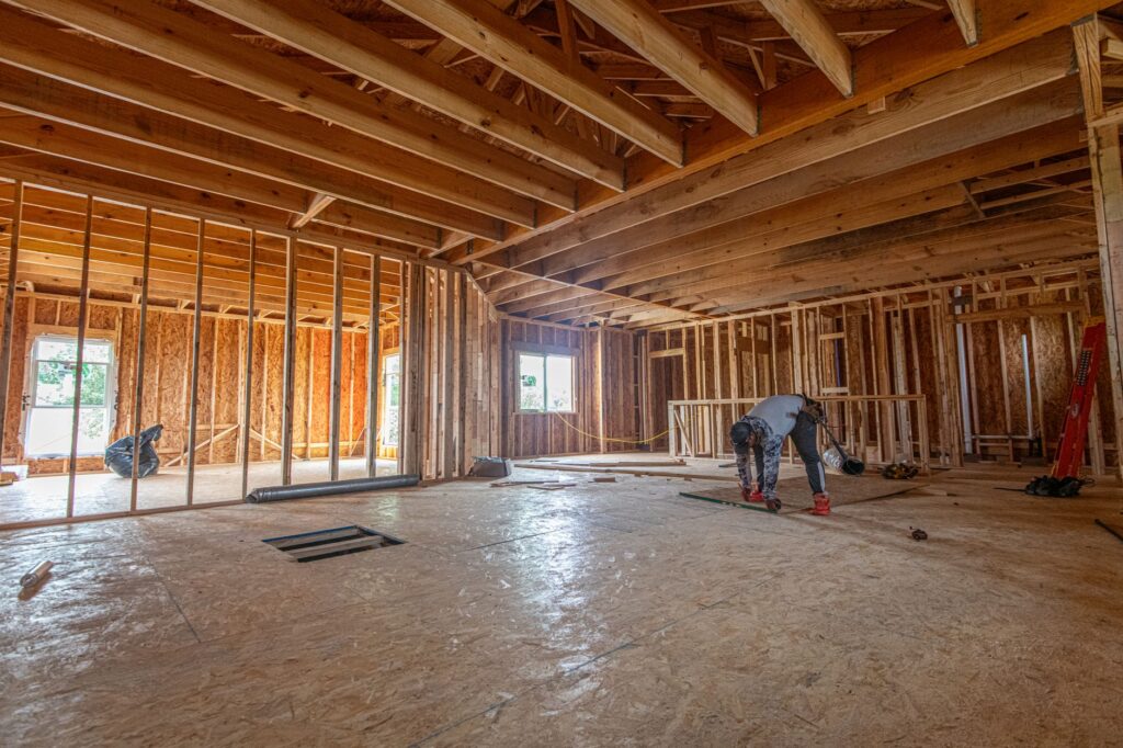 Construction crew framing the foundation and walls of a modern new home under a clear sky.